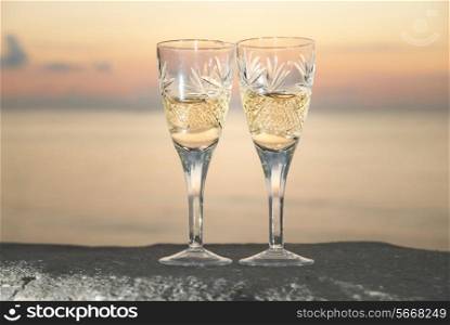Two wedding glasses with champagne over sunset