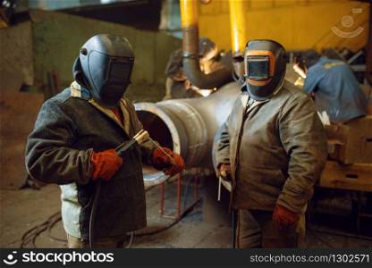 Two welder in masks prepares to work with metal construction on factory, welding skill. Metalworking industry, industrial manufacturing of steel products. Two welder in masks prepares to work with metal