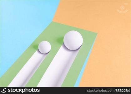 Two white balls roll downhill and leave a trail on a multicolor background. Abstract minimal concept. Isometric rectangle with copy space. Geometric shapes.. Two white balls roll downhill and leave a trail on a multicolor background