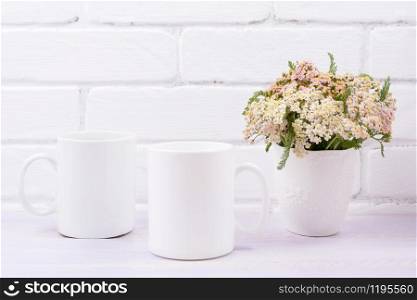 Two white coffee mug mockup with pink beige wild flowers in the vase. Empty mug mock up for design promotion.