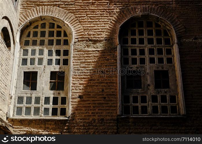 Two windows in shade and light on tile brick wall
