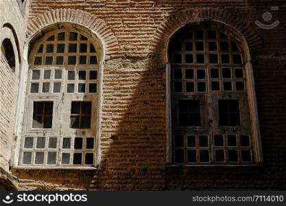 Two windows in shade and light on tile brick wall