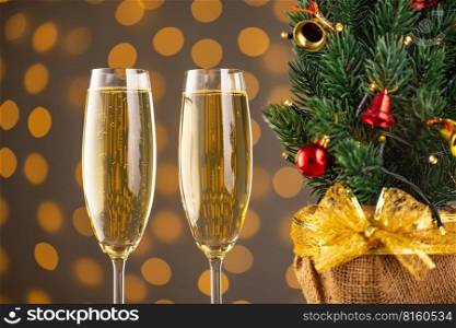 Two wine glasses with bubbly champagne and Christmas tree with decor on background of blurry sparkling lights. Happy New Year holiday greeting card, banner, header with copy space 