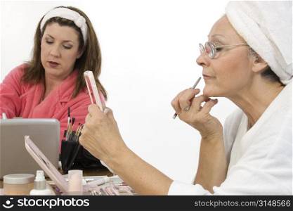 Two woman (30&acute;s and 50&acute;s) putting on make-up together. Shot in studio over white.