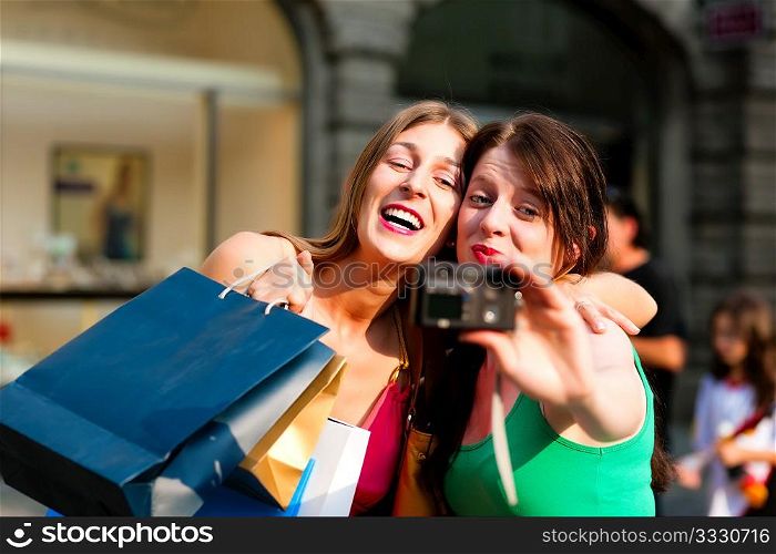 Two woman being friends shopping downtown with colourful shopping bags and taking a picture from themselves
