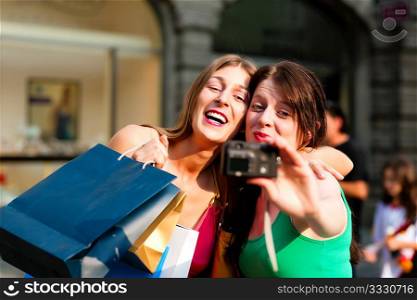 Two woman being friends shopping downtown with colourful shopping bags and taking a picture from themselves