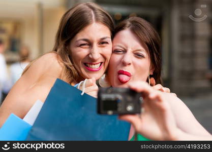 Two woman being friends shopping downtown with colourful shopping bags and taking a picture from themselves