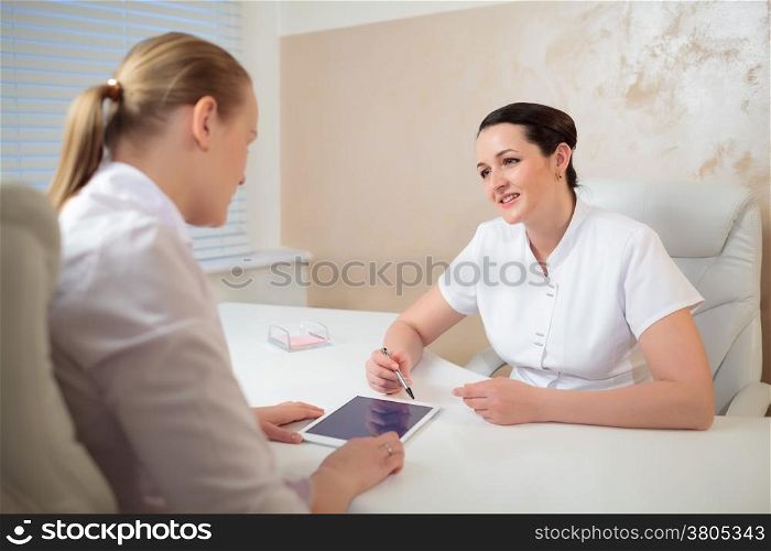 Two woman cosmeticians in the office room having a professional talk using pad