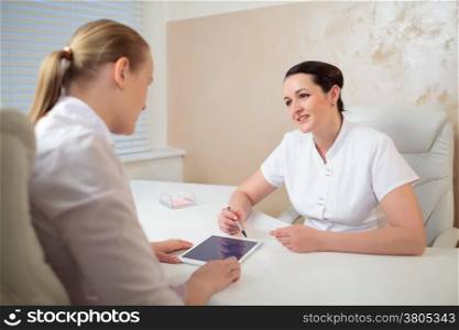 Two woman cosmeticians in the office room having a professional talk using pad