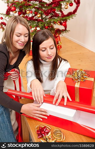 Two woman packing Christmas present in front of tree