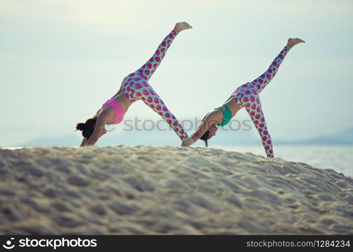 two woman playing yoga on sea beach