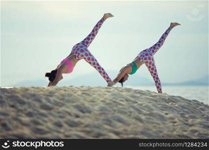two woman playing yoga on sea beach