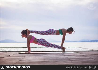 two woman playing yoga pose on beach pier