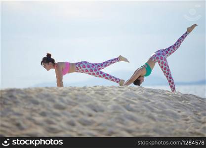 two woman playing yoga pose on sea beach