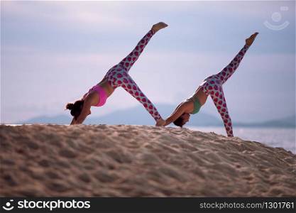 two woman posing yoga on sea beach