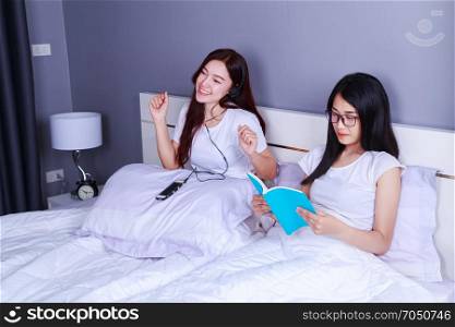 two woman reading a book and using smart phone on bed in the bedroom
