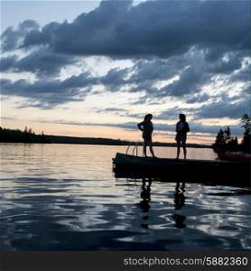 Two Woman standing on dock at dusk, Lake of the Woods, Ontario, Canada