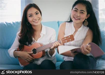 Two women are having fun playing ukulele and smiling at home for relax time