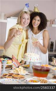 Two women at party holding drinks standing by food table smiling