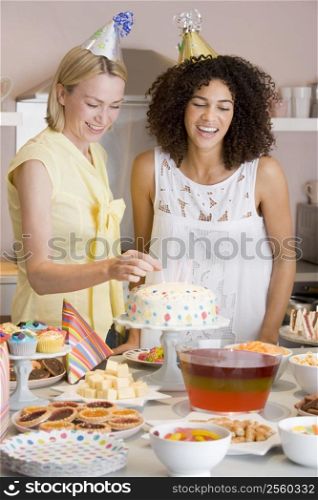 Two women at party putting candles in cake smiling