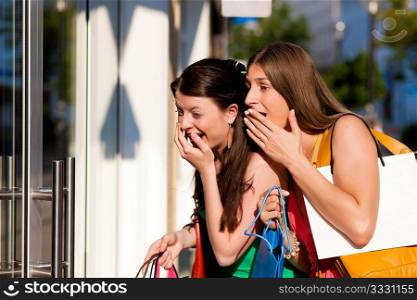 Two women being friends shopping downtown with colorful shopping bags, they are lolling into a store window and are amazed