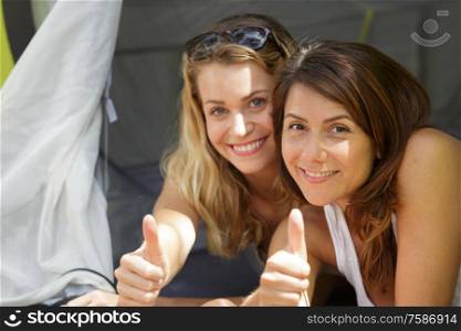 two women camping and showing thumbs up