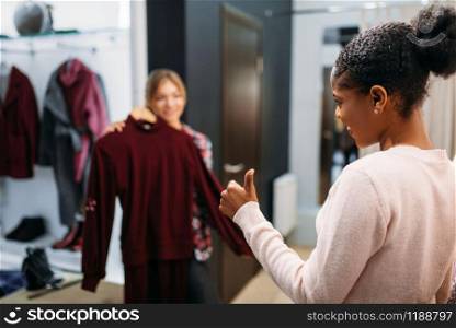 Two women choosing clothes, shopping. Shopaholics in clothing store, consumerism lifestyle, fashion. Two women choosing clothes, shopping