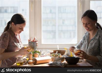 Two women cooking pizza at home. Filling pizza with ingredients