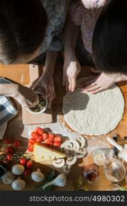 Two women cooking pizza at home. Filling pizza with ingredients. Top view. Overhead view.