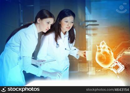 Two women doctors. Image of two attractive women cardiologist examining virtual heart