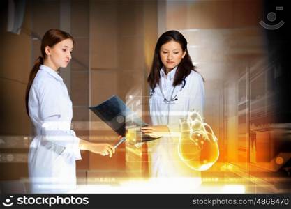 Two women doctors. Image of two attractive women cardiologist examining virtual heart