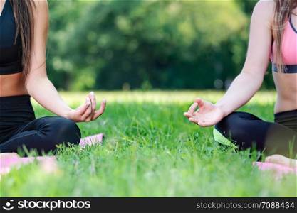 Two women doing yoga meditation in a lotus pose outdoors in a park on a sunny day in close-up (copy space)