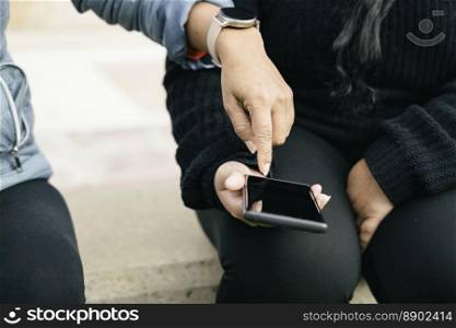 two women dressed in black clothes, using smart electronic devices, smart phone and smart watch, sharing information from social networks and online shops.. woman&rsquo;s hand with smart watch pointing to smart phone, holding in her hand young latina woman, front view without recognisable faces