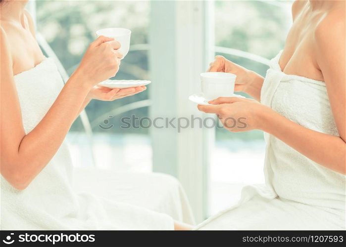 Two women drinking tea or herbal drinks while having conversation in luxury day spa. Wellness, leisure and healthcare concept.