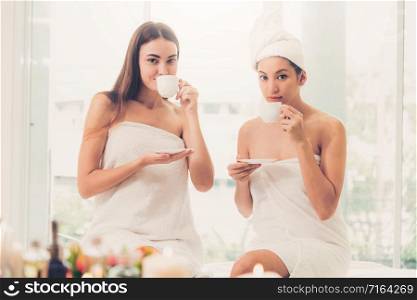 Two women drinking tea or herbal drinks while having conversation in luxury day spa. Wellness, leisure and healthcare concept.. Two women drinking tea in luxury day spa.