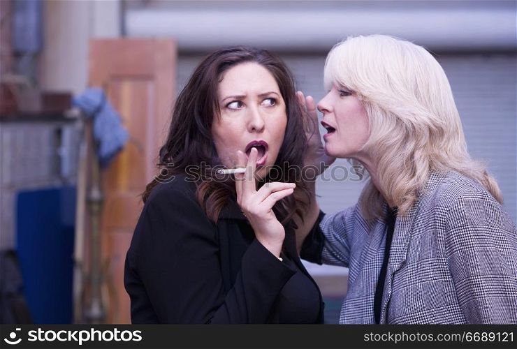 Two women engaging in gossip during a smoking break