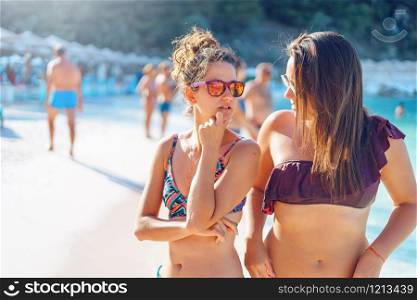 Two women female girls sisters or friends couple talking on the beach in the bikini swim suit in sunny summer day wearing sunglasses on the vacation