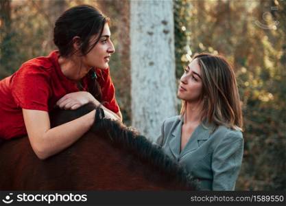Two women friends chatting and taking a ride with their horse through the countryside