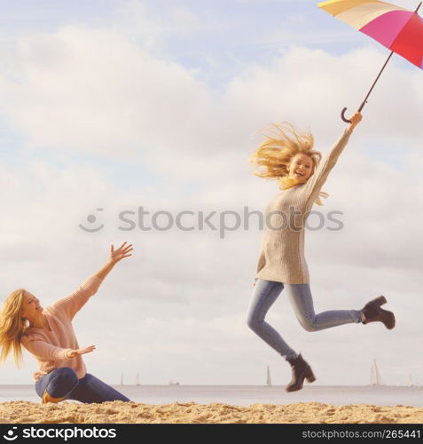 Two women full of joy jumping around with colorful umbrella. Female friends having fun outdoor.. Women jumping with umbrella