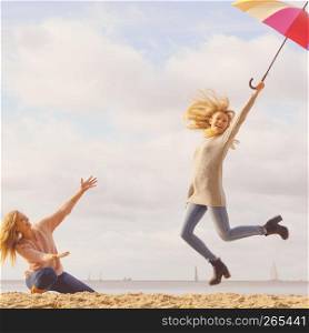 Two women full of joy jumping around with colorful umbrella. Female friends having fun outdoor.. Women jumping with umbrella