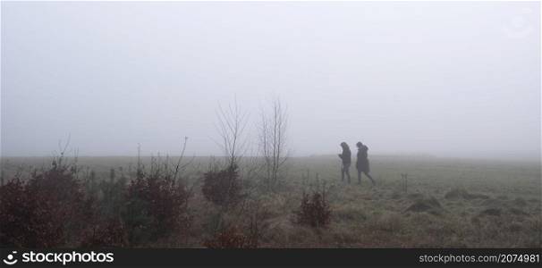 two women hike on foggy day in winter on grassy field in the netherlands near utrecht