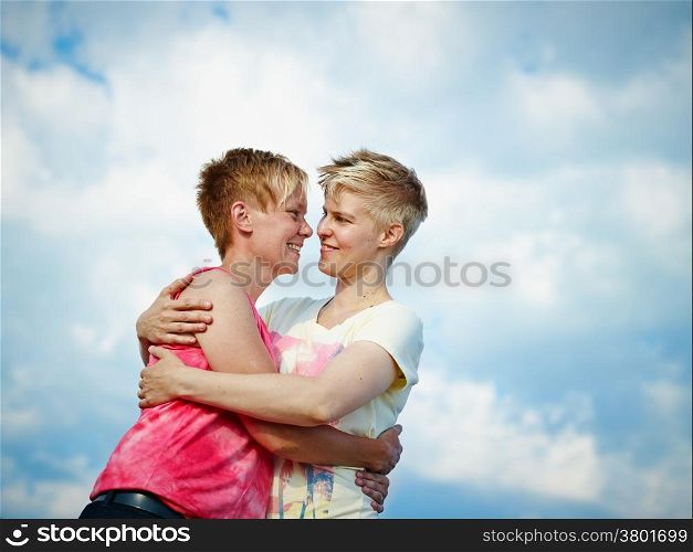 Two women hugging in the afternoon sunlight, cloudy sky on background