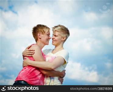 Two women hugging in the afternoon sunlight, cloudy sky on background