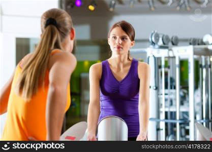 Two women in gym in front of a exercising machine having a chat