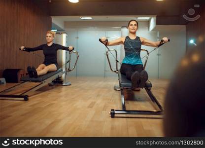 Two women in sportswear, pilates training on exercise machine in gym. Fitness workuot in sport club. Athletic female person, aerobics indoor, body stretching. Two women in sportswear, pilates training in gym
