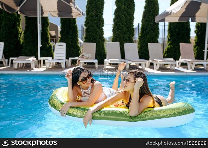 Two women in sunglasses sunbathing on inflatable mattress in the pool on resort. Beautiful girls relax at the poolside in sunny day, summer holidays of attractive ladies. Women in sunglasses sunbathing on mattress in pool