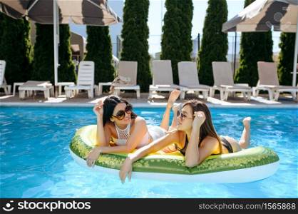 Two women in sunglasses sunbathing on inflatable mattress in the pool on resort. Beautiful girls relax at the poolside in sunny day, summer holidays of attractive ladies. Women in sunglasses sunbathing on mattress in pool