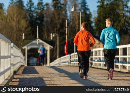 Two women jogging together along the bridge at sunrise