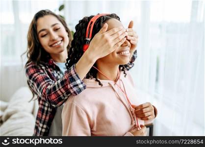 Two women jokes and listening to music at home. Pretty girlfriends in earphones relax in the room, sound lovers resting on couch, female friends leisures together. Two women jokes and listening to music