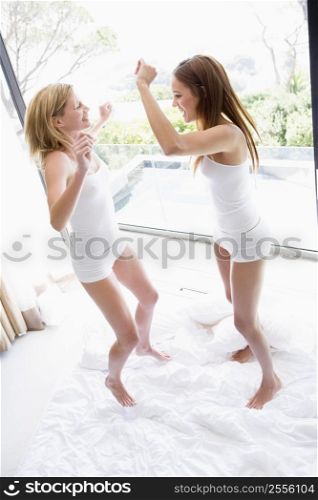 Two women jumping on bed smiling